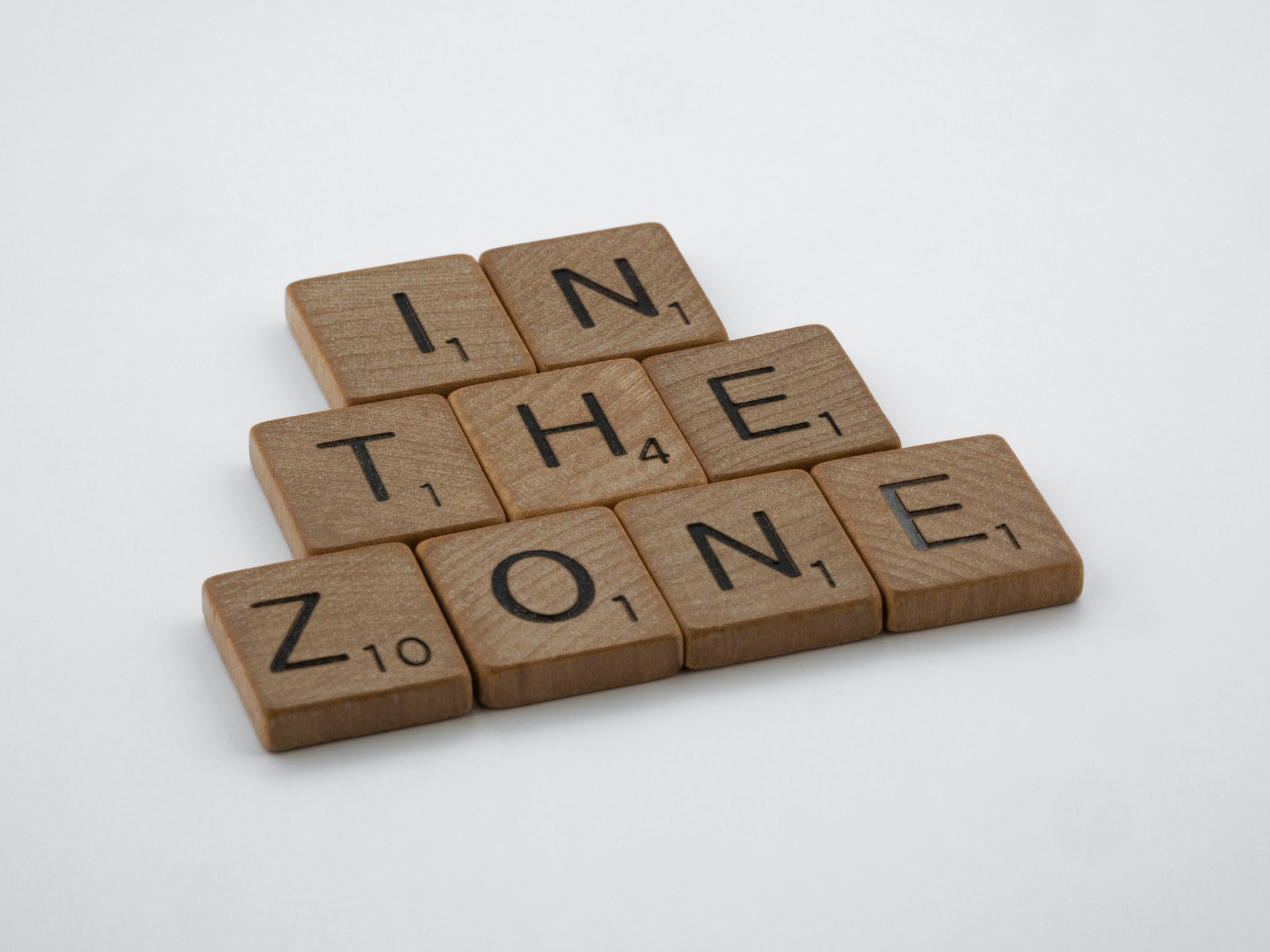Wooden Scrabble tiles are arranged in three lines, spelling out the words 'IN THE ZONE'