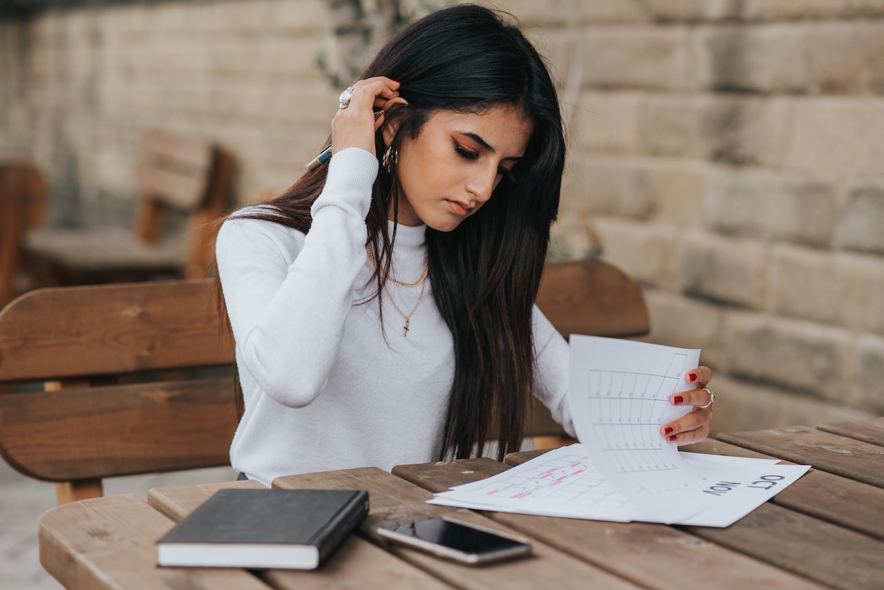 A woman sitting at a desk looking through papers with one hand and putting her hair behind her ear with her other hand