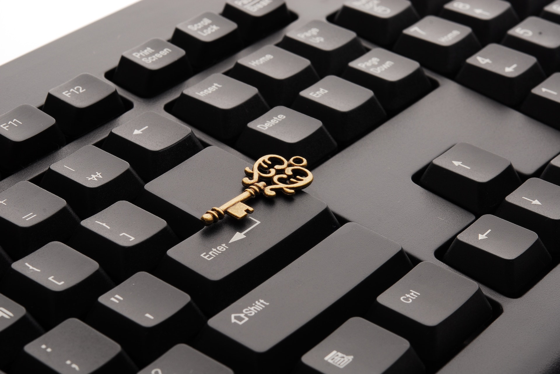 A section of a black computer keyboard at an angle with an ornate golden key on top of the keys.
