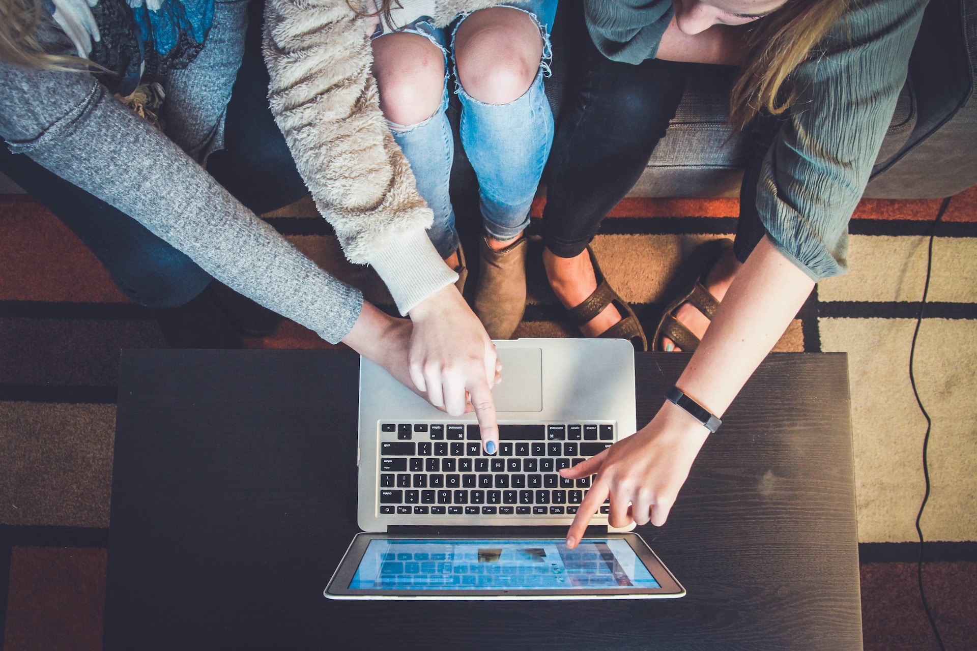 A view from above of three women sitting on a sofa pointing at a website that's displayed on an open laptop on a table in front of them
