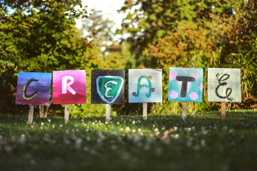 Wooden signs staked into the grass, each with a colourful letter painted on it, spelling the word 'CREATE'.