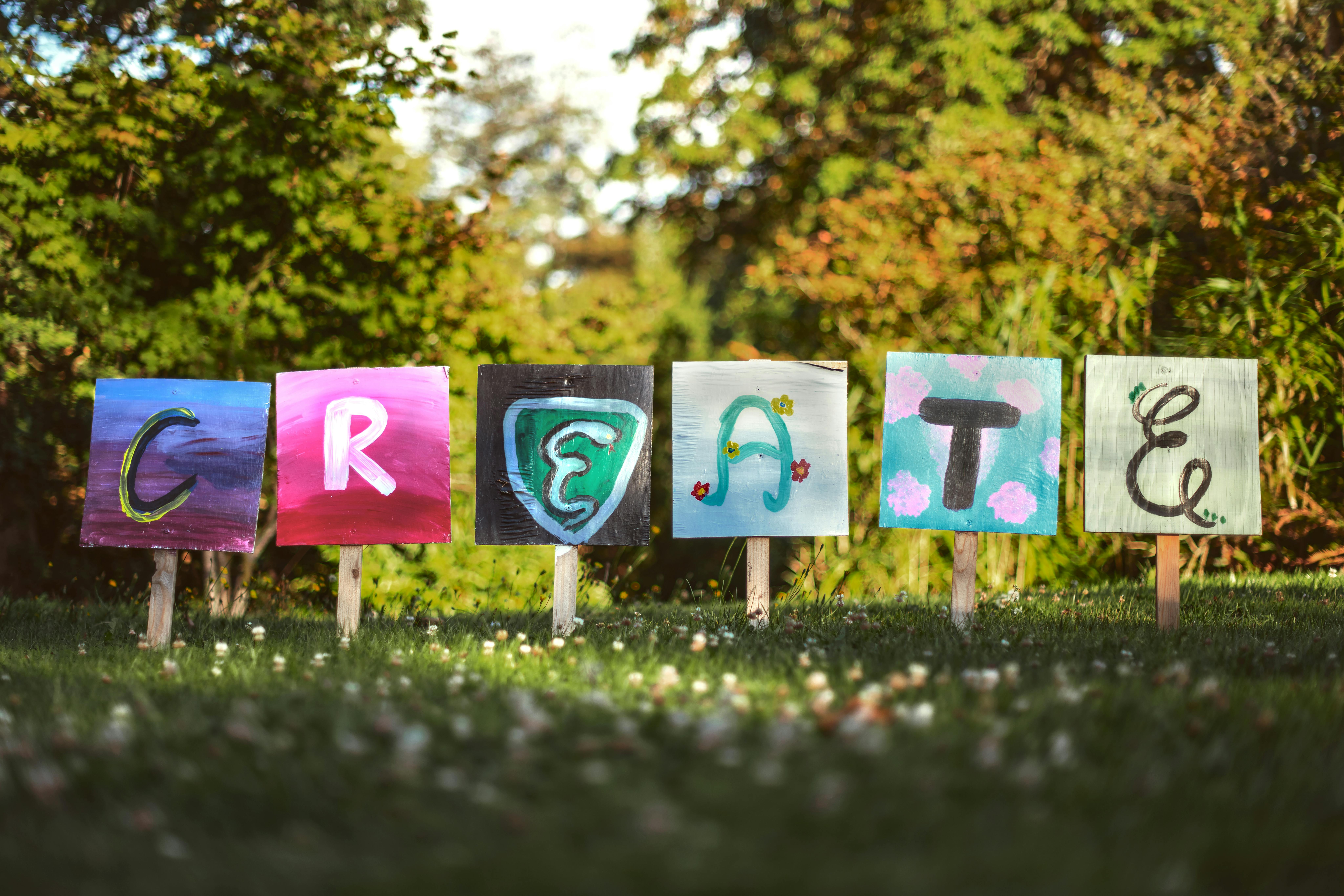 Wooden signs staked into the grass, each with a colourful letter painted on it, spelling the word 'CREATE'.