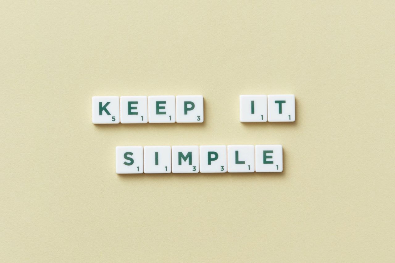 White scrabble tiles set in two rows against a pale yellow background, spelling out the words 'KEEP IT SIMPLE'