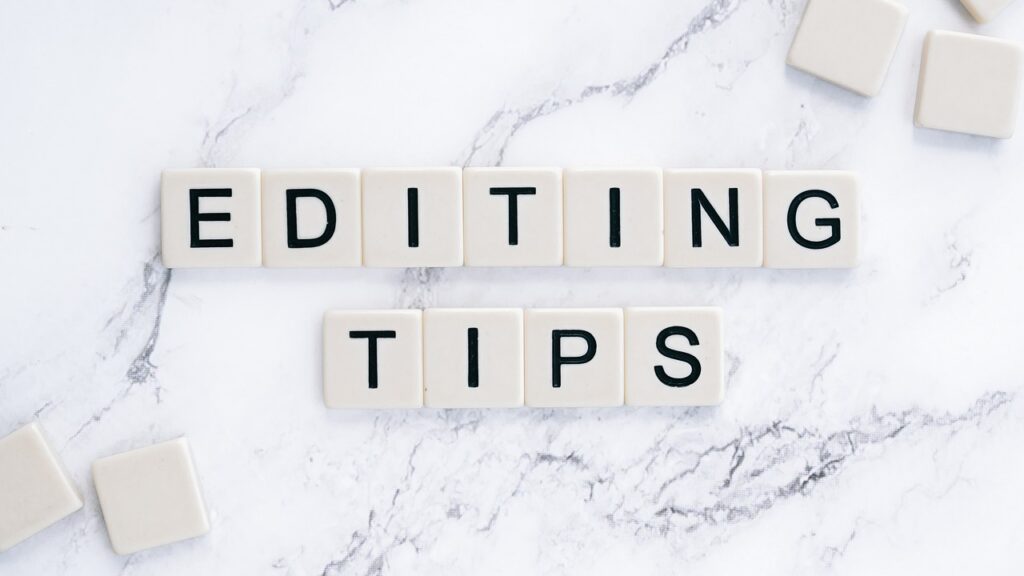 White Scrabble tiles in two rows on a marble surface, spelling the words 'EDITING TIPS'