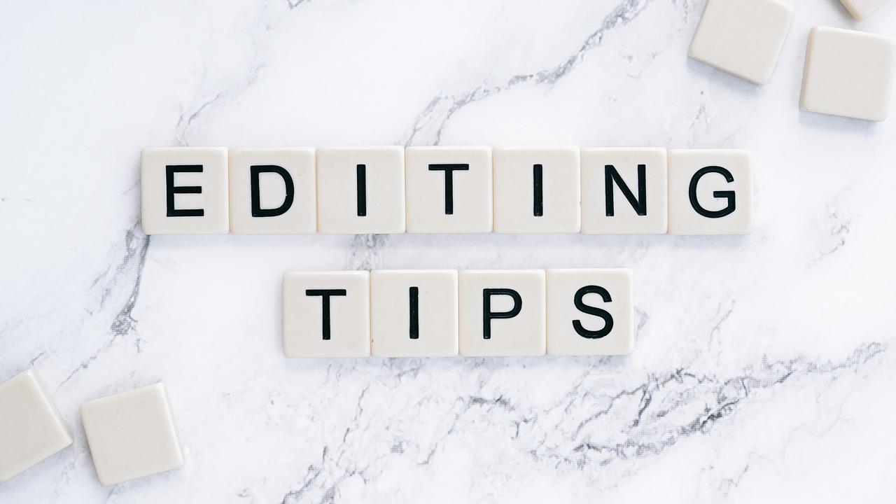 White Scrabble tiles in two rows on a marble surface, spelling the words 'EDITING TIPS'