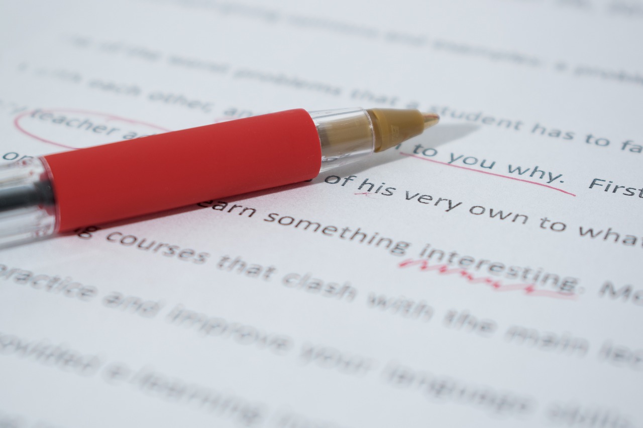 A red biro on top of a piece of paper where the text has been edited in red ink.