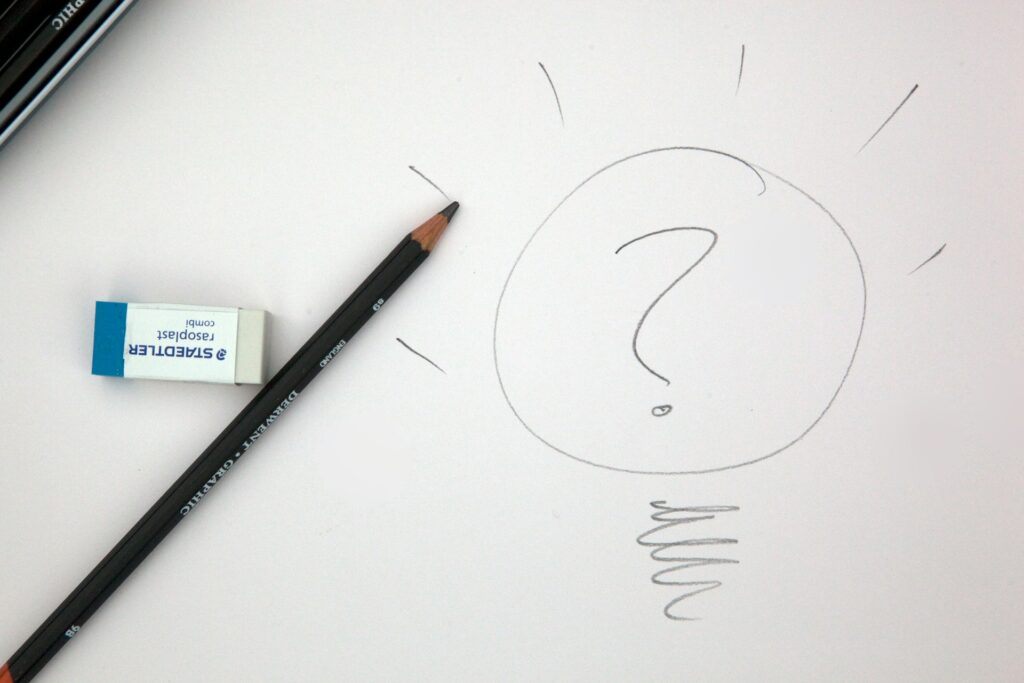 A pencil and eraser on a white piece of paper next to a hand-drawn picture showing a question mark in a circle with small lines emanating from the circle.