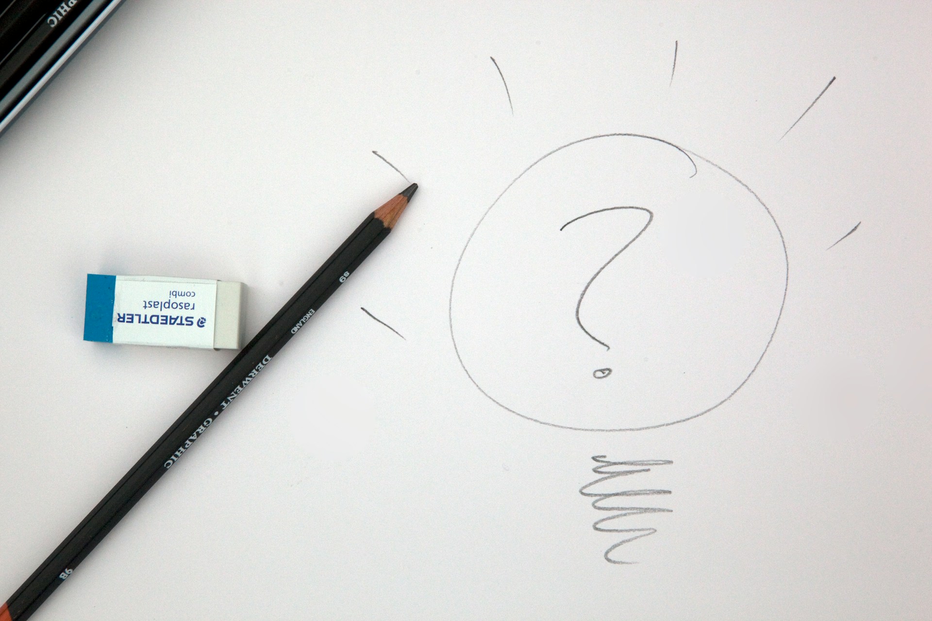 A pencil and eraser on a white piece of paper next to a hand-drawn picture showing a question mark in a circle with small lines emanating from the circle.